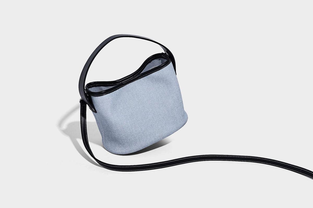 Hellblaue Bucket-Bag aus Denim mit schwarzem Besatz in Lederoptik, silberfarbenen Beschlägen, kurzem Tragegriff und langem verstellbarem Crossbody-Riemen