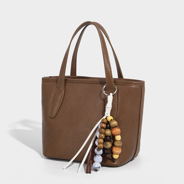 Compact structured bucket tote bag with pebbled textured finish, dual top handles, silver-tone lock hardware, and detachable