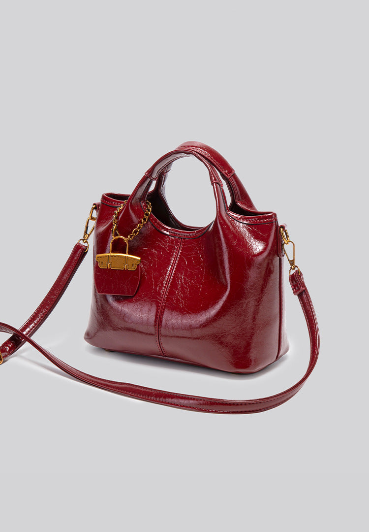 Structured crinkle-gloss top-handle satchel in deep burgundy with antique gold lock charm and detachable shoulder strap