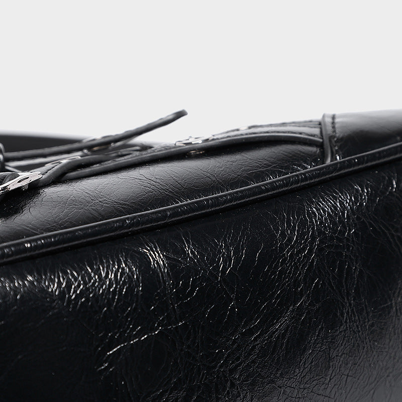 Compact moto-inspired shoulder bag with crisscross grommet strap detail, glossy textured finish, and adjustable crossbody