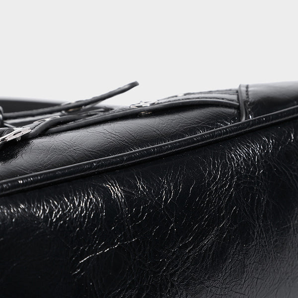 Compact moto-inspired shoulder bag with crisscross grommet strap detail, glossy textured finish, and adjustable crossbody