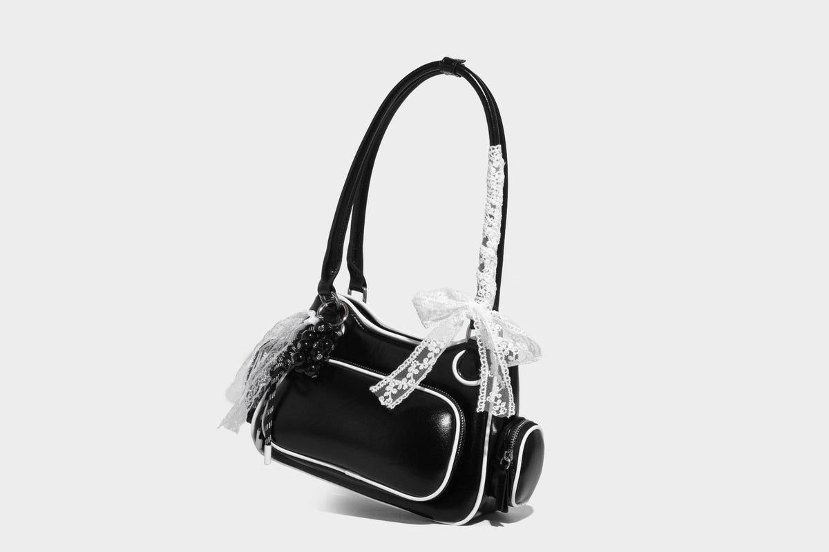 Kleine, formstabile Schultertasche mit glänzender Oberfläche, weißem Paspelbesatz, Spitzenschleife und rotem Perlenanhänger, Reißverschluss-Seitentaschen und silberfarbenem