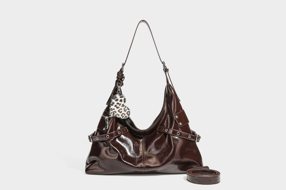 Glänzende dunkelbraune, lässig geschnittene Hobo-Schultertasche mit Riemendetail mit silberfarbenen Ösen, Reißverschlussfach auf der Vorderseite und Herz mit Leopardenmuster