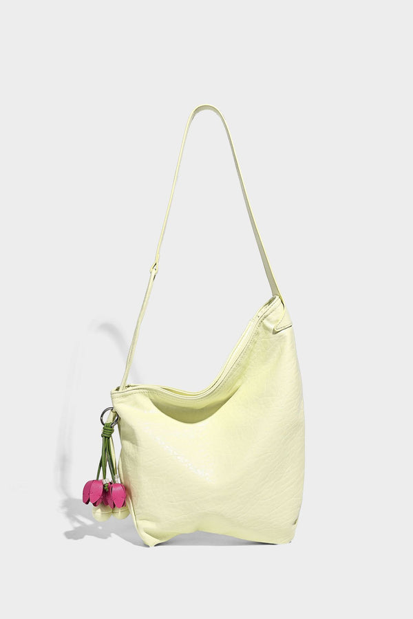 Slouchy hobo shoulder bag in pale yellow with slim strap, drawstring bead closure, and pink tulip floral charm, detail view