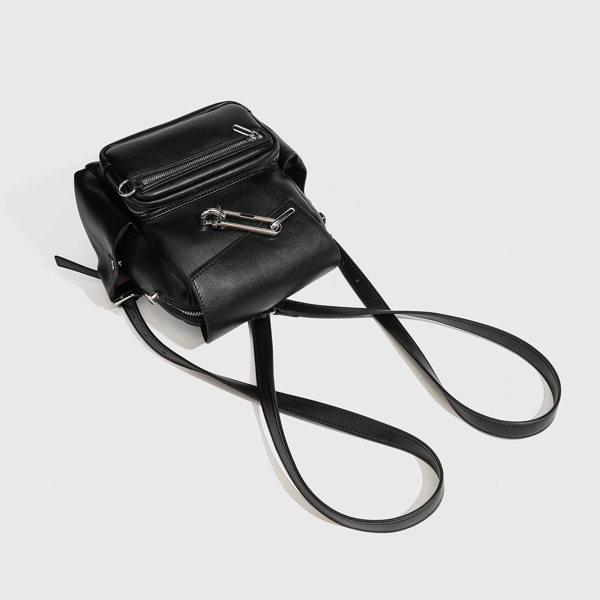 Kleiner strukturierter Rucksack aus Material in schwarzer Lederoptik mit Überschlag, Metallverschluss in Silberoptik, vorderem Reißverschlussfach und Ring