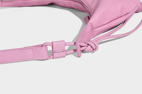 Slouchy crescent half-moon shoulder bag in pink pebbled textured finish with floral charm and knotted side detail, detail
