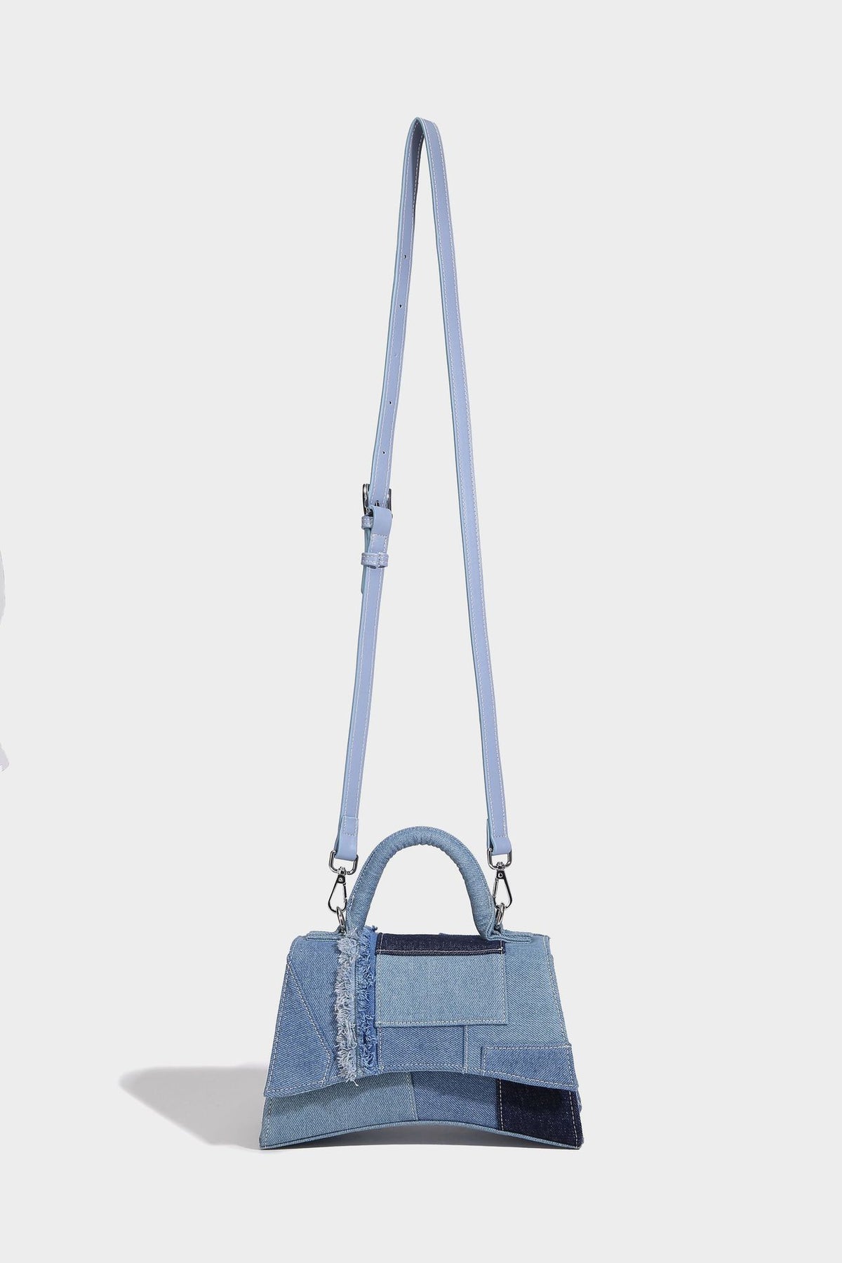 Structured patchwork denim trapezoid satchel bag with frayed panel trim, rounded top handle, and silver-tone hardware, detail