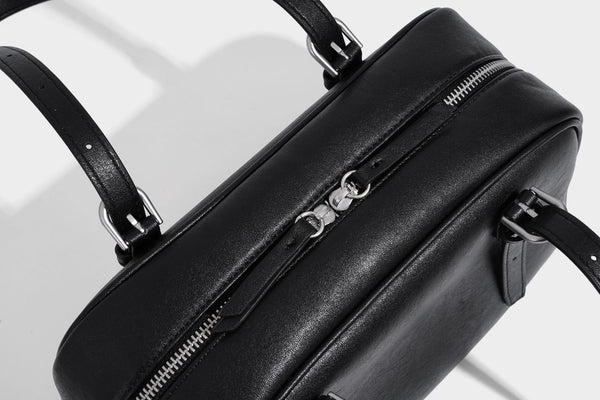 Structured dome-shaped shoulder bag with leather-look finish, top zipper closure, dual adjustable slim straps, and, detail
