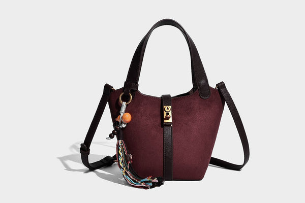 Small structured trapezoid tote bag in matte suede-look finish with black contrast trim, gold-tone front clasp, tassel charm