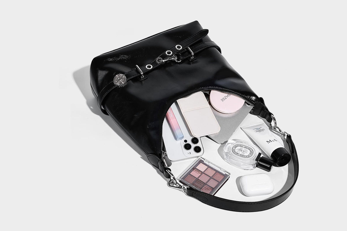 Glossy black slouchy hobo shoulder bag with silver-tone hardware, belt-style grommet strap at base, and long adjustable