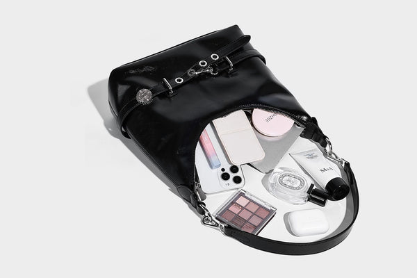 Glossy black slouchy hobo shoulder bag with silver-tone hardware, belt-style grommet strap at base, and long adjustable
