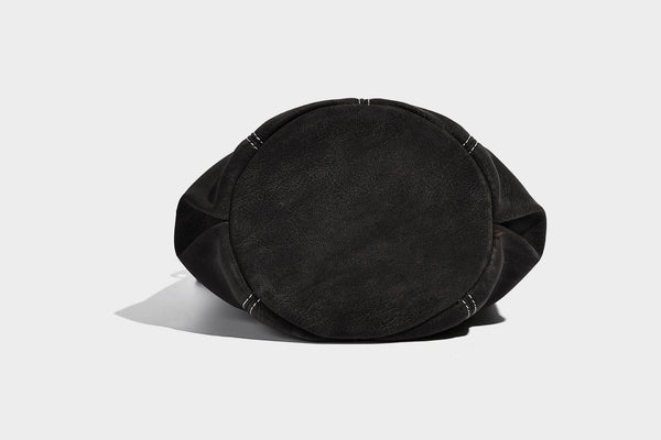 Small matte textured bucket crossbody bag with flap closure, gold-tone bar hardware, contrast stitching, and pompom tassel