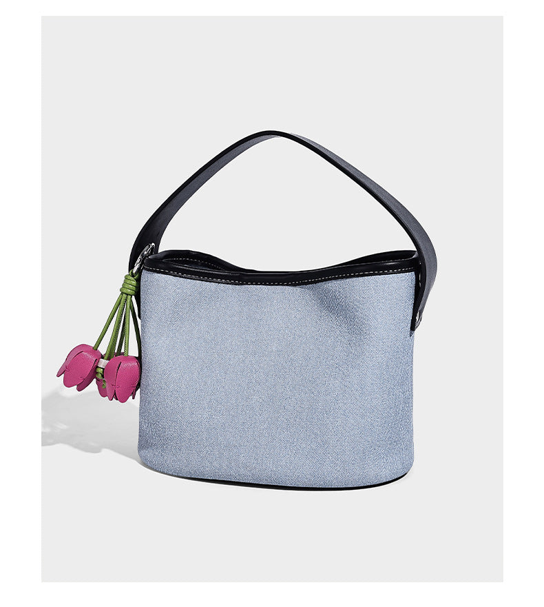 Small denim-look bucket bag with black leather-look trim, pink tulip flower charm, and adjustable crossbody strap, detail