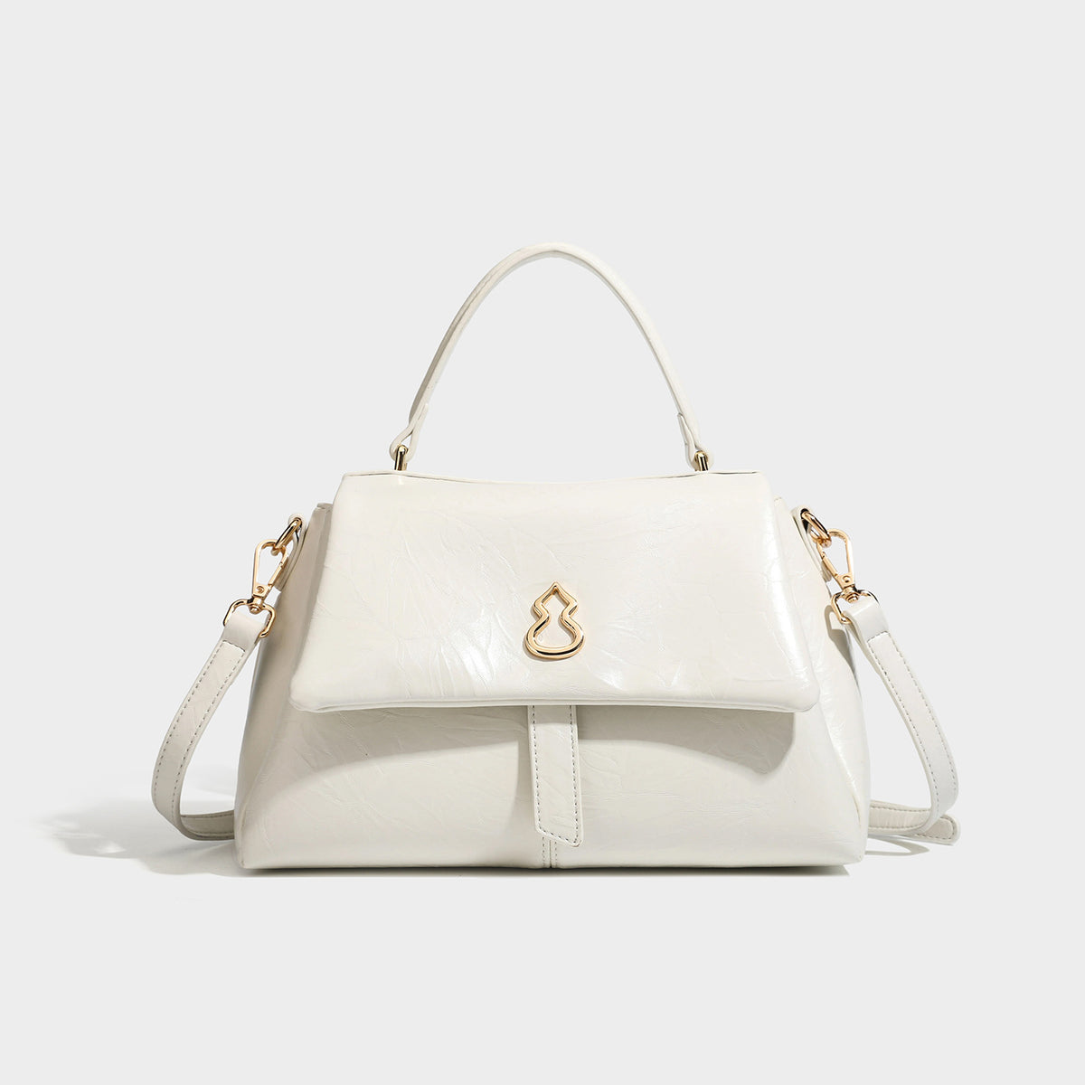 Structured black satchel bag with glossy crinkled leather-look finish, gold-tone emblem flap closure, slim top handle, and