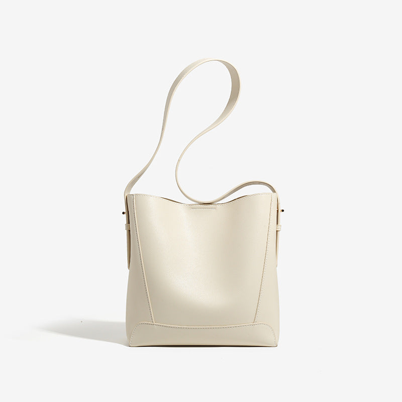 Structured smooth leather-look bucket shoulder bag with long adjustable strap and gold-tone buckle hardware in brown, detail