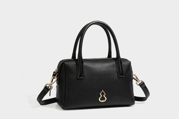 Small structured pillow satchel bag with pebbled leather-look finish, dual rolled top handles, gold-tone gourd emblem, and