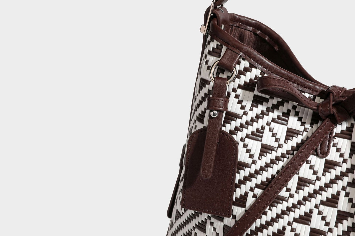 Woven geometric bucket shoulder bag in white and dark brown two-tone pattern with leather-look trim and drawstring top