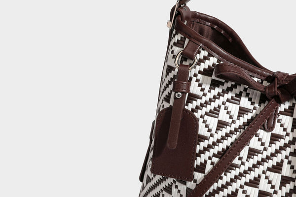Woven geometric bucket shoulder bag in white and dark brown two-tone pattern with leather-look trim and drawstring top