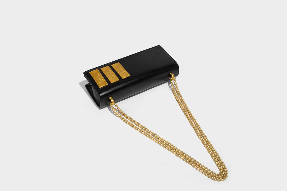 Structured rectangular crossbody bag with glossy finish, three vertical gold-tone embossed plaques, and gold chain strap