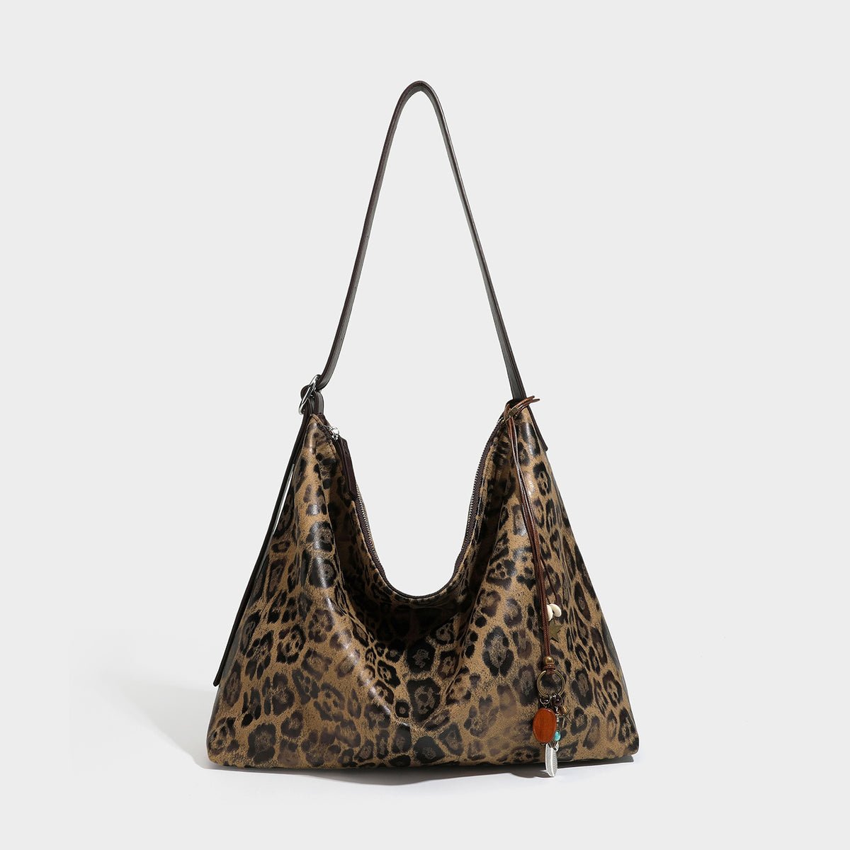 Slouchy leopard print hobo shoulder bag with glossy coated finish, top zipper closure, dark brown trim, and dangling charm