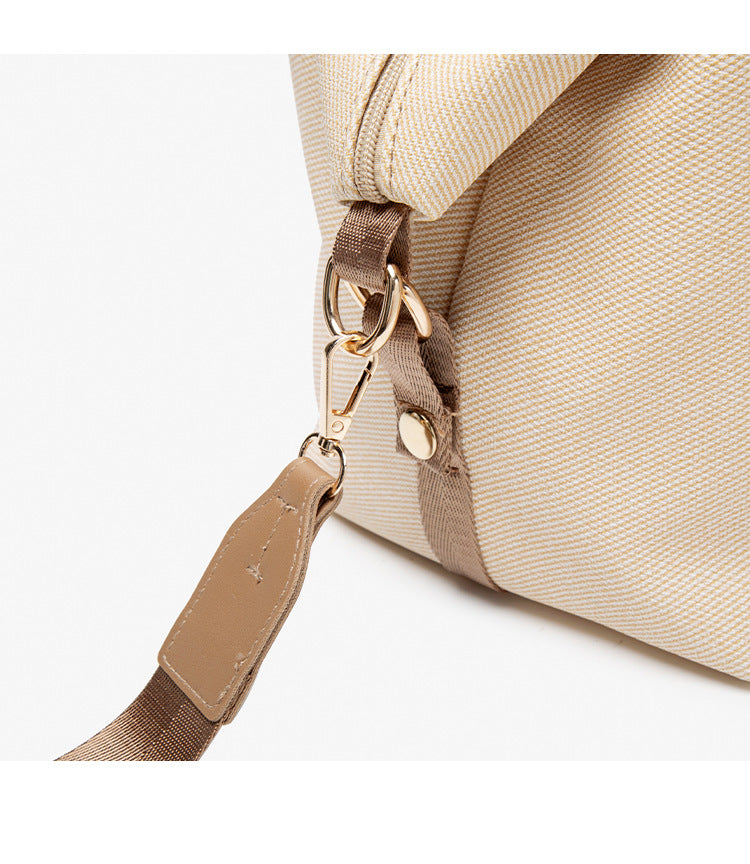 Structured woven duffel bag with dual tan webbing handles, detachable shoulder strap, top zip closure, and gold-tone