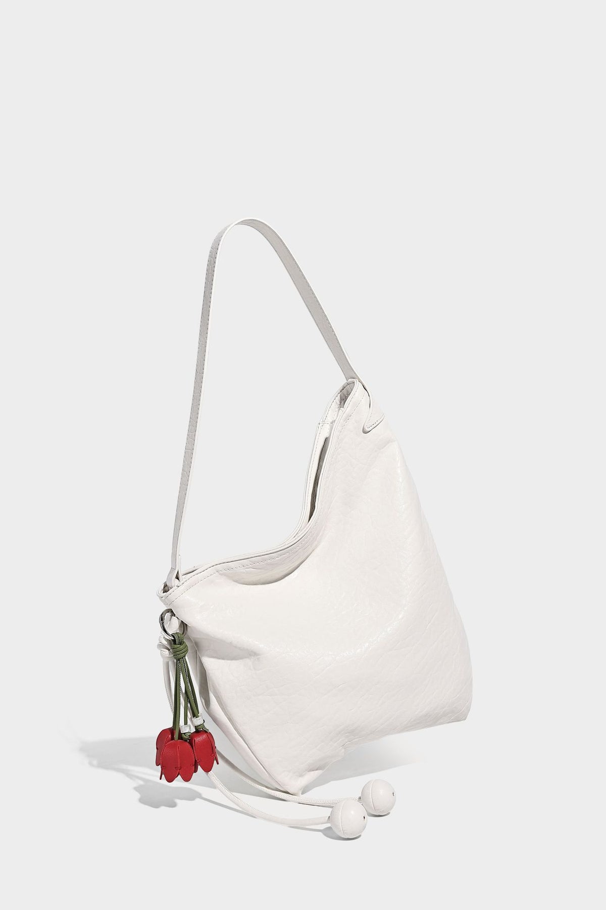 Slouchy hobo shoulder bag in pale yellow with slim strap, drawstring bead closure, and pink tulip floral charm, detail view