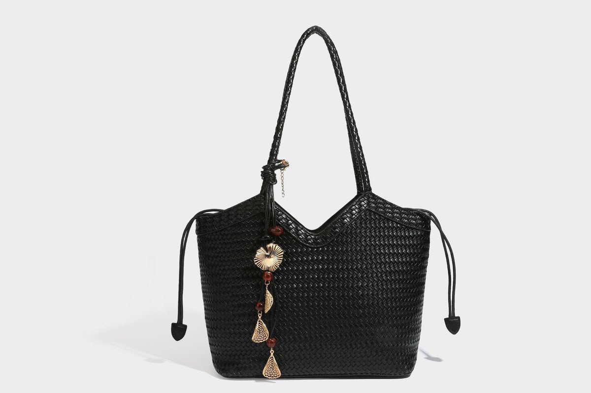 Olivgrüne Tote-Bag in Korbgeflecht-Optik mit dunkelbraunen geflochtenen Schulterriemen, seitlichen Kordelzügen und Perlenanhänger in Goldoptik