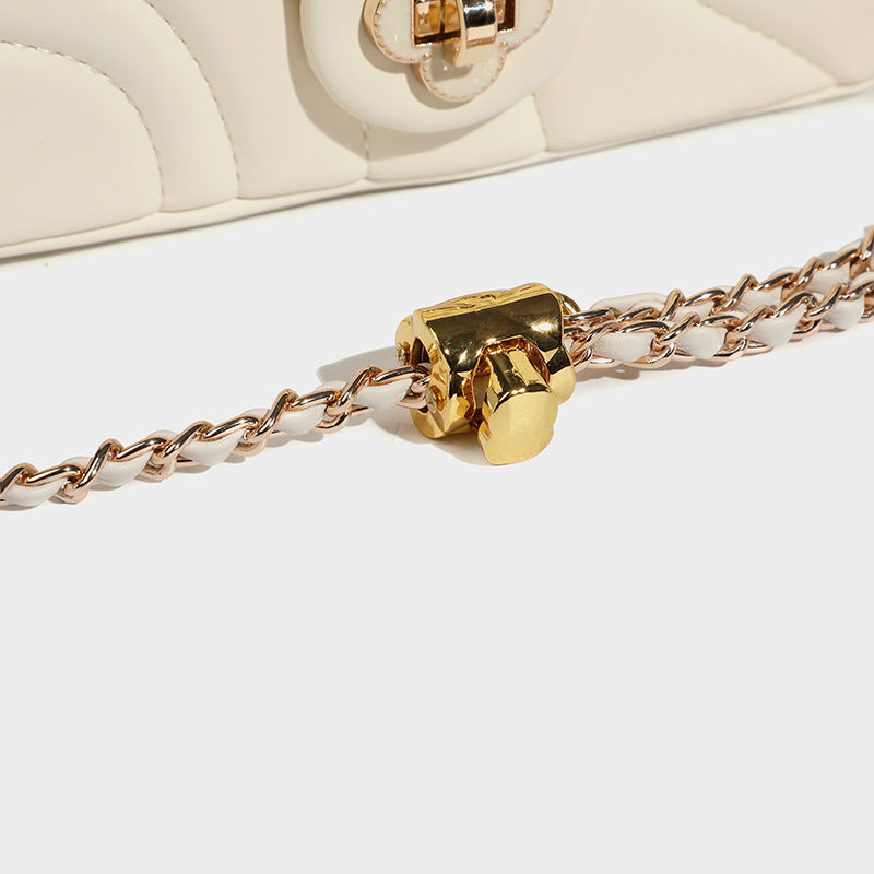 Compact cream quilted flap crossbody bag with wave stitching, gold-tone chain strap, and four-petal turn-lock clasp, detail