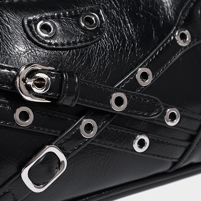 Compact moto-inspired shoulder bag with crisscross grommet strap detail, glossy textured finish, and adjustable crossbody