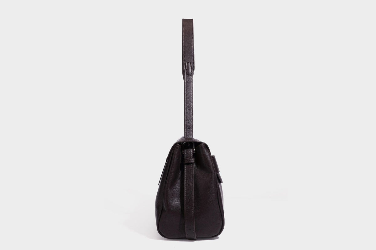 Strukturierte rechteckige dunkelbraune Schultertasche in Lederoptik mit Klappe, mehrlagigem Detail auf der Vorderseite und langem verstellbarem Riemen, Detailansicht