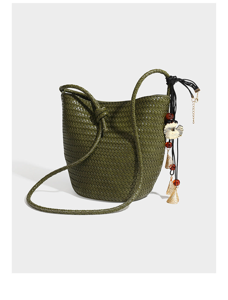 Olive green woven leather-look bucket bag with braided crossbody strap, knotted adjustment, and gold-tone tassel charm with