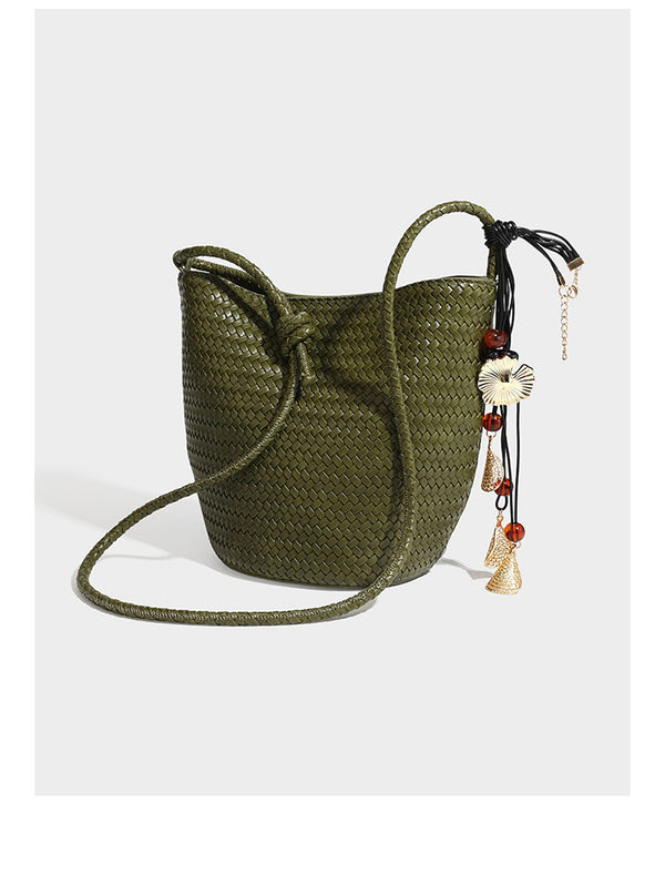 Olive green woven leather-look bucket bag with braided crossbody strap, knotted adjustment, and gold-tone tassel charm with