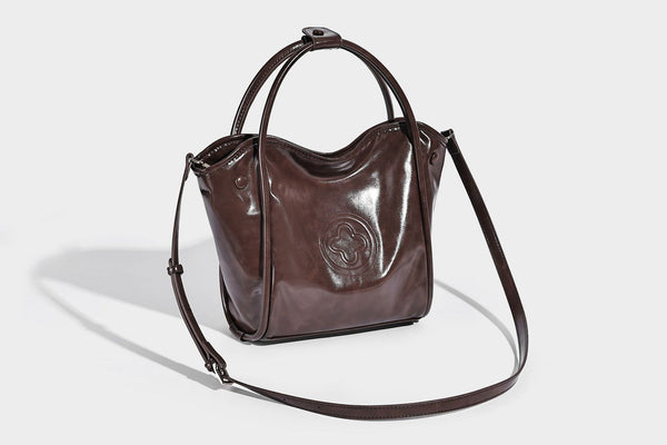 Glossy leather-look structured tote bag with rounded top handles, detachable shoulder strap, embossed front emblem, and side