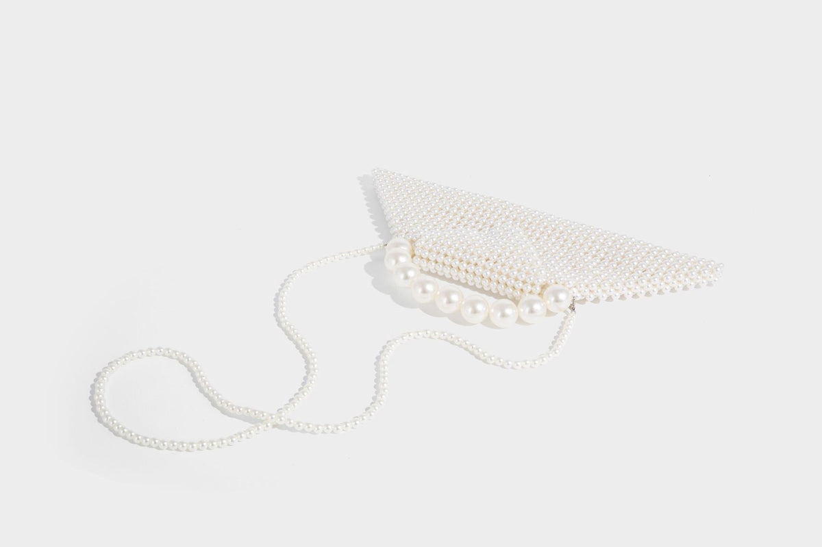 Small structured triangle clutch bag covered in glossy pearl beads with an arched pearl top handle and silver snap closure