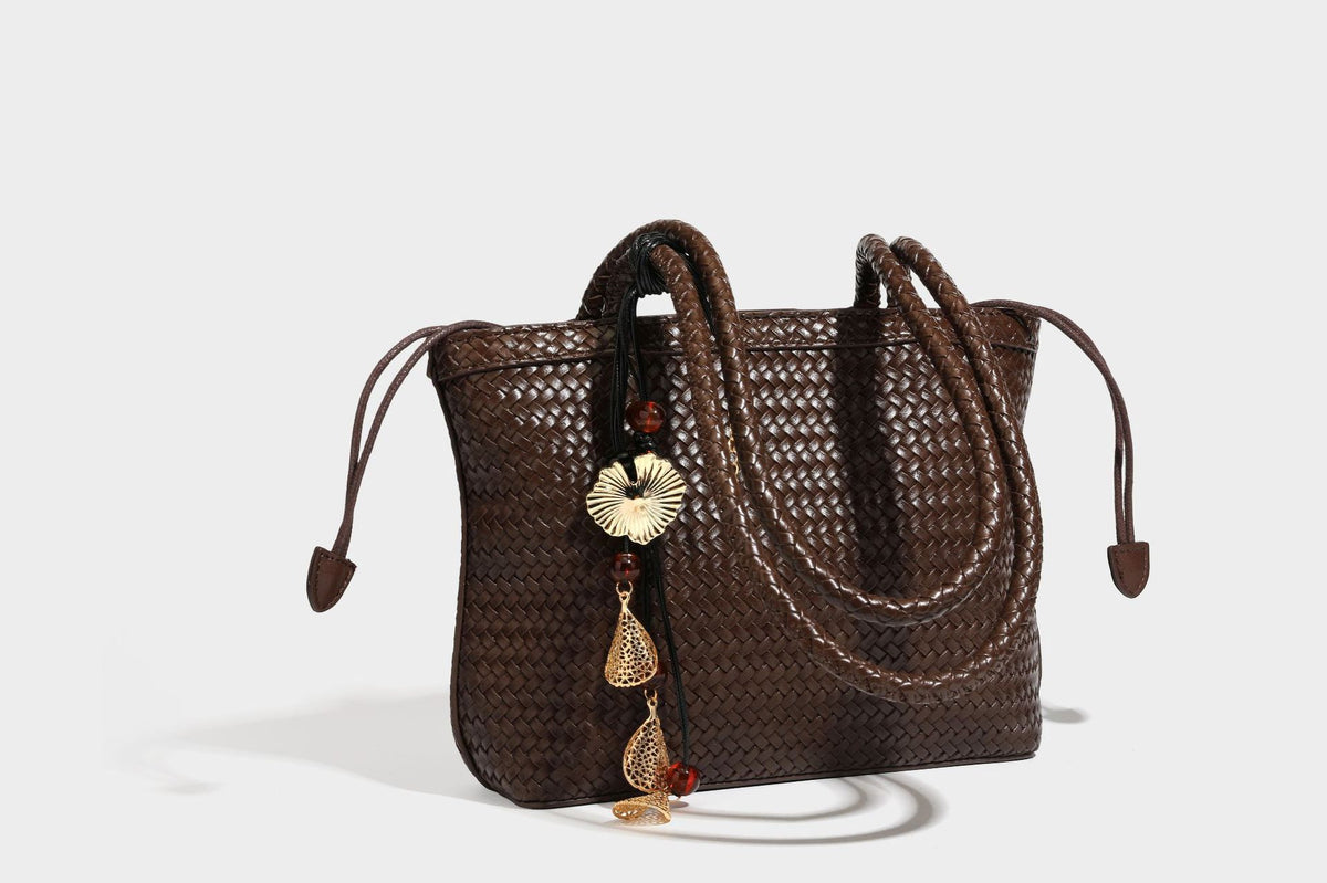 Structured woven leather-look tote bag in dark brown with long shoulder straps, side drawstring ties, and gold filigree