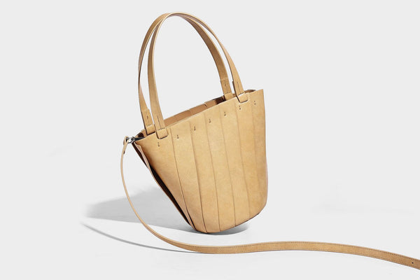 Structured bucket tote bag with vertical panel exterior, dual top handles, and detachable shoulder strap in tan leather-look