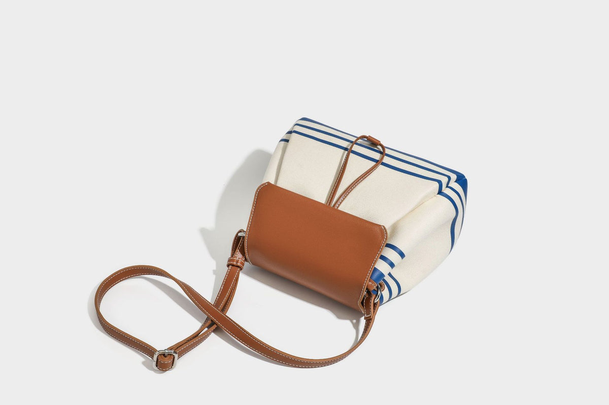 Cream canvas bucket bag with blue horizontal stripes, tan leather-look flap and trim, drawstring closure, silver-tone, detail