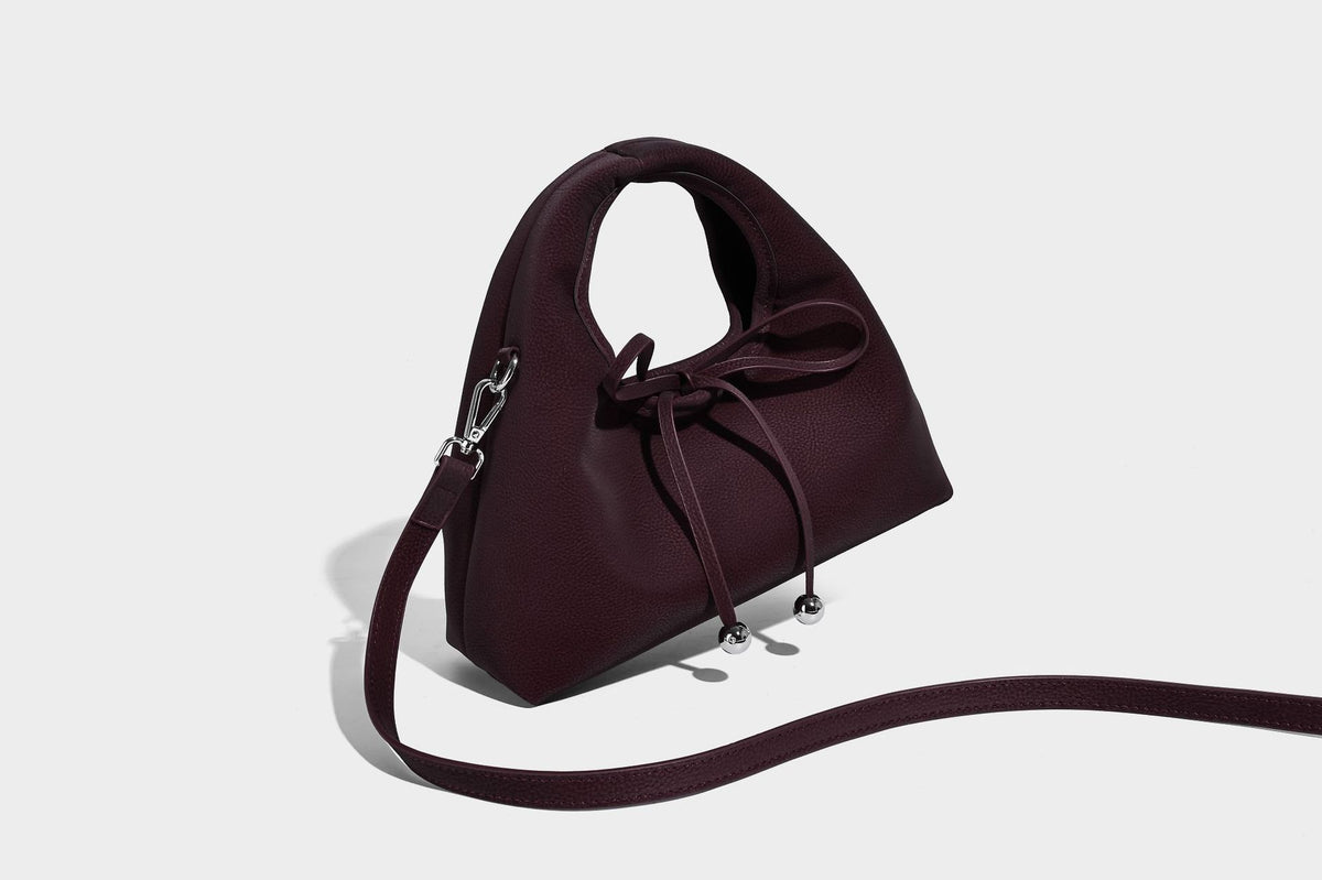 Pebbled matte trapezoid top-handle bag with drawstring bow closure, bead-tipped cords, silver-tone hardware, and detachable