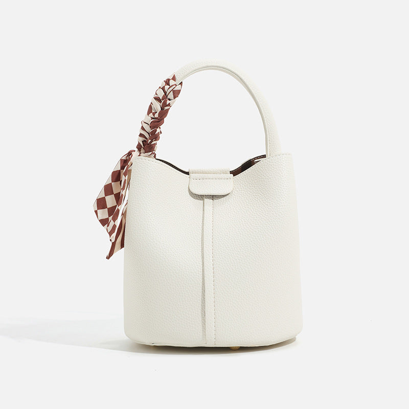 Pebbled leather-look bucket bag with checkered scarf-wrapped top handle, flap tab closure, gold-tone hardware, and matching