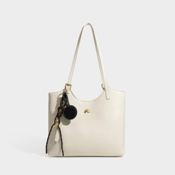 Structured smooth leather-look tote bag with long shoulder strap, gold-tone hardware, and hanging tassel-coin charm, detail