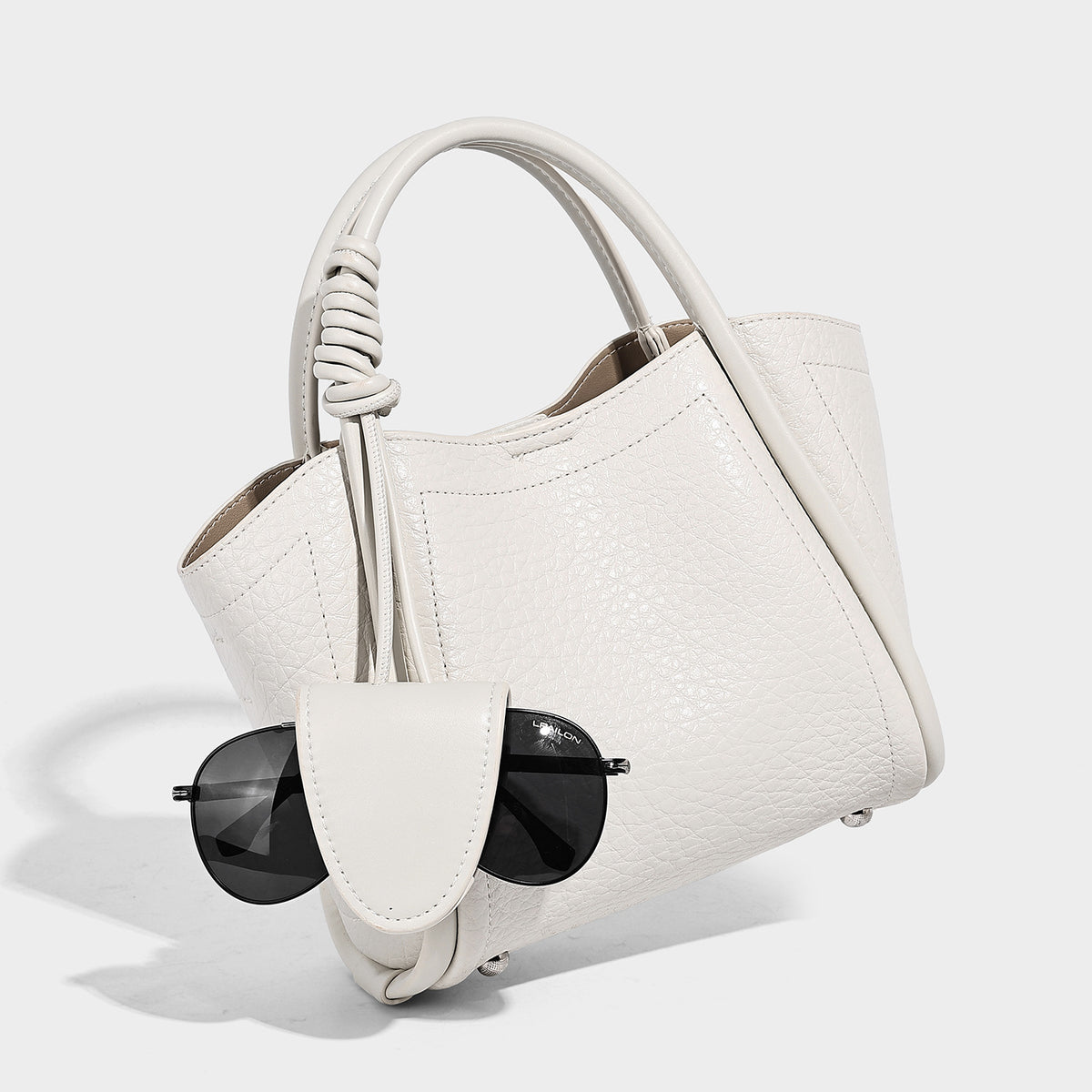 Structured mini tote bag in pebbled leather-look finish with knotted top handles, front flap pocket, and detachable shoulder