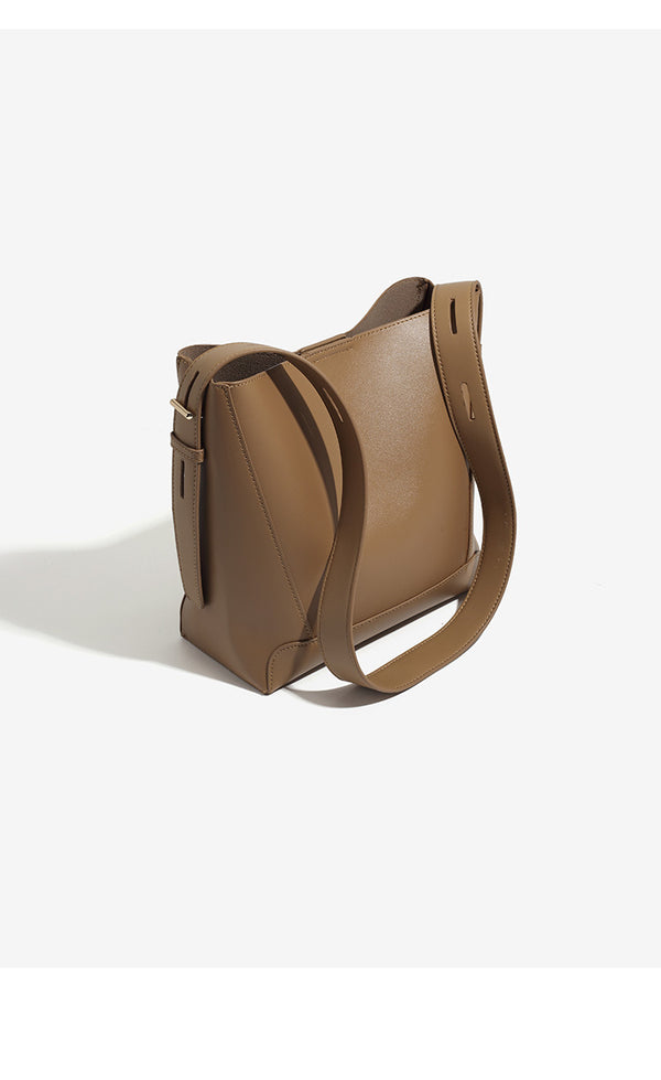 Structured smooth leather-look bucket shoulder bag with long adjustable strap and gold-tone buckle hardware in brown, detail