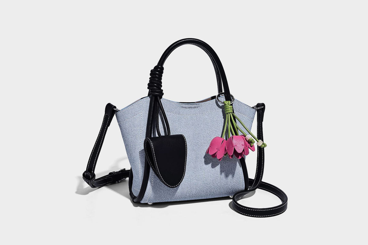 Light blue denim trapezoid tote bag with black leather-look trim, knotted top handles, detachable crossbody strap, front