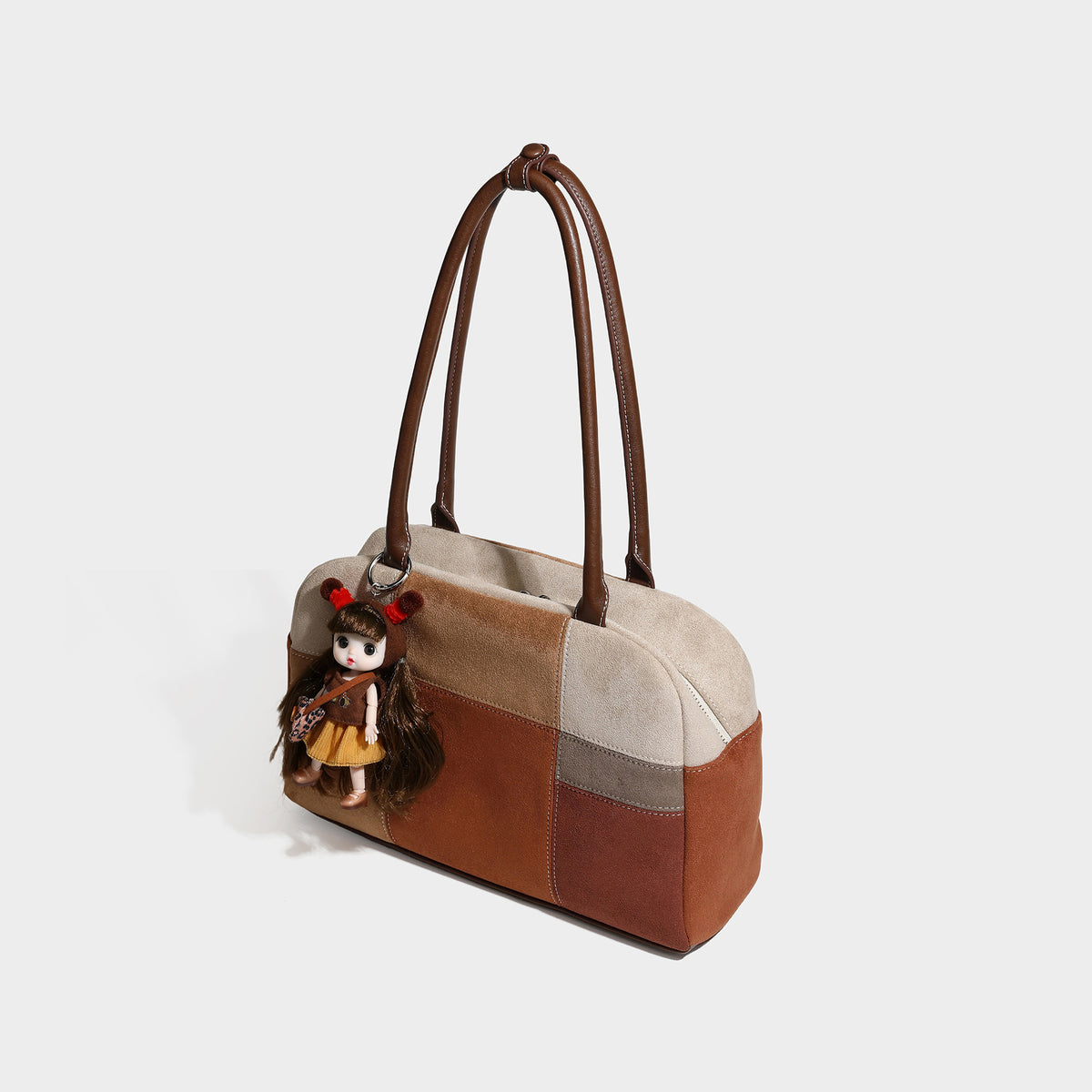 Boxy patchwork suede-look shoulder tote in tan, beige, rust, and brown panels with double brown straps and hanging doll