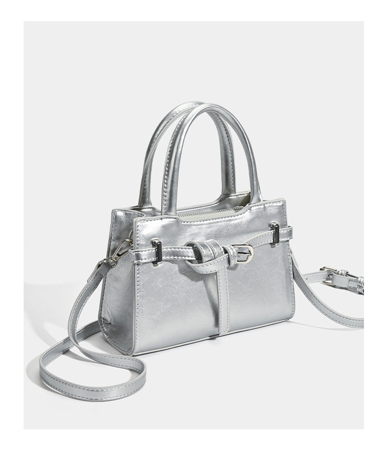 Small structured trapezoid mini top-handle bag with front belt-knot buckle detail and glossy leather-look finish, detail view