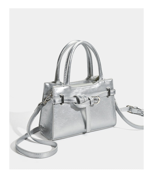 Small structured trapezoid mini top-handle bag with front belt-knot buckle detail and glossy leather-look finish, detail view