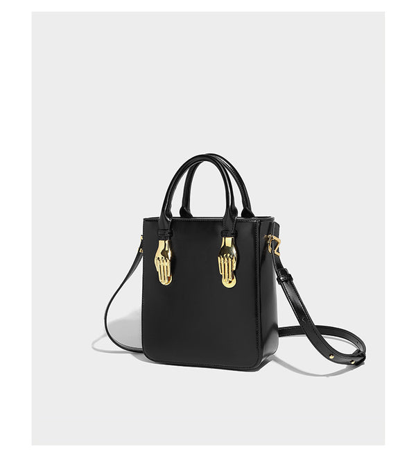 Kleine, strukturierte, kastenförmige Henkeltasche mit goldfarbenem, handförmigem Metallbeschlag in schwarzer Lederoptik mit abnehmbarem Detail