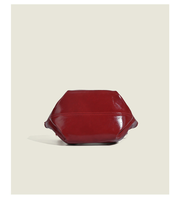 Small structured red glossy PU handbag with bow-and-bead charm, dual top handles, and detachable crossbody strap, detail view
