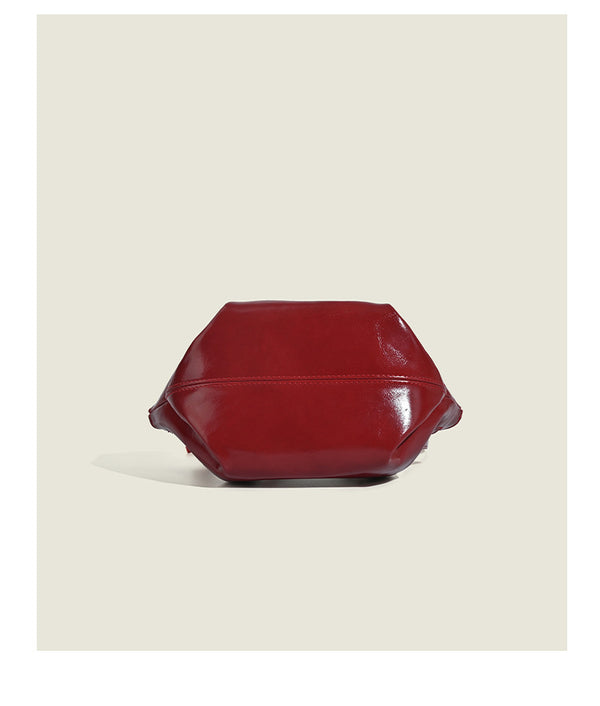 Small structured red glossy PU handbag with bow-and-bead charm, dual top handles, and detachable crossbody strap, detail view