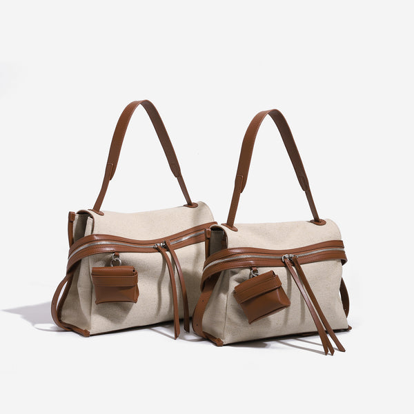 Cream canvas zip-top shoulder bag with cognac leather-look trim, dual zipper, attached mini pouch, and tassel strap ties